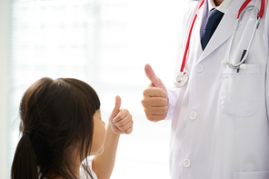 Unknown doctor and little girl hands with thumbs up .