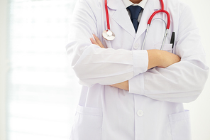 Unknow doctor posing with arms crossed in the office, he is wearing a stethoscope .