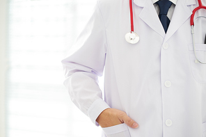 Unknown doctor posing  hand in pocket in the office, he is wearing a stethoscope .