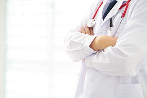 Unknow doctor posing with arms crossed in the office, he is wearing a stethoscope .