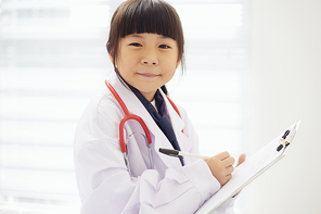 Portrait of little girl dressed as a doctor with a stethoscope and taking notes with bright background .