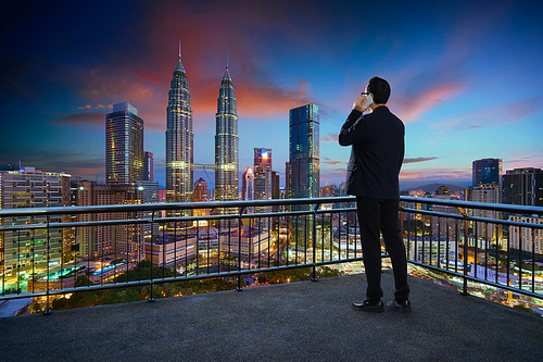 Young businessman standing on a balcony  using smartphone with beautiful city skyline background . Night scene .