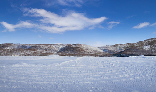 Snow fields with tire tracks and beautiful landscape with hills, blue sky and white clouds