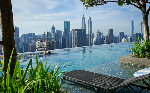 Kuala Lumpur, Malaysia - Feb, 21, 2023 : Girl swim in swimming pool on roof top with beautiful city view of the skyscrapers