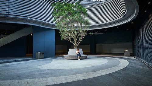 Businesswoman playing with mobile phone while sitting in public area outside modern architecture