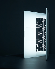 An open, illuminated laptop casts a soft light in a dark, moody setting