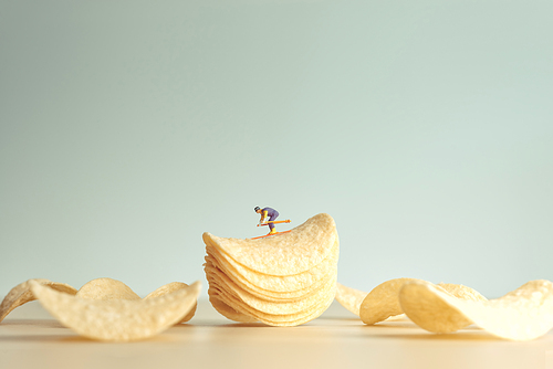 Miniature skier skiing down potatoe chips.