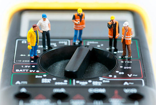 Team of miniature workers on top of multimeter. Macro photo