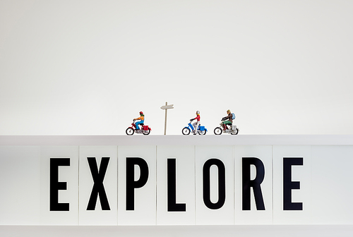 Miniature travellers ride over lightbox with the word Explore.
