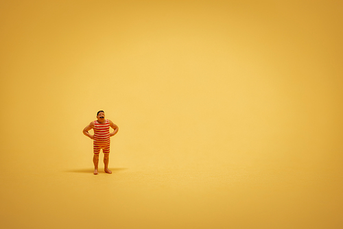 Miniature guy in retro swimsuit on yellow backgound with some copyspace.