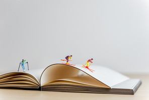 Miniature skiers sliding down the open book. Sport and travel concept.