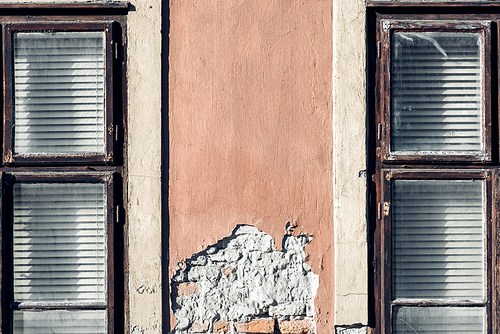 Two windows on the facade of an old house with peeling plaster