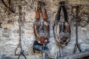 Old worn saddle hanging from an old barn stone wall.