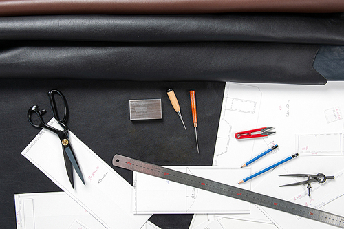 테이블위에 설계도와 가죽과 줄자 가위 연필