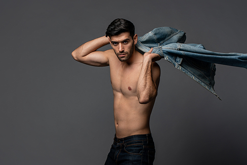 Young handsome sexy shirtless man with denim jacket posing in light gray isolated studio background