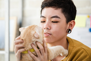 Close up shot of young Asian tomboy woman in casual attire hold and look at her cat affectionately