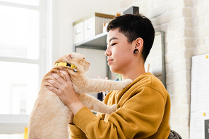 Young Asian tomboy woman in casual attire holding and looking at her cat affectionately