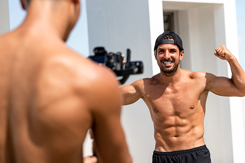 Handsome man fitness vlogger flexing his arm muscles while recording exercise video clip outdoors