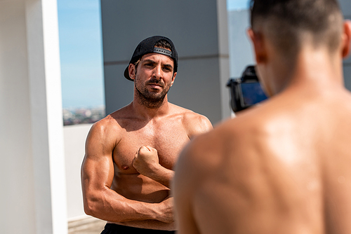 Handsome man fitness vlogger flexing his arm muscles while recording exercise video clip outdoors