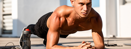 Banner image of handsome muscular sports man doing plank exercise outdoors on rooftop