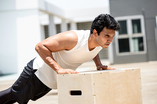 Handsome Indian sports man doing push up exercise outdoors on building rooftop, home workout concept