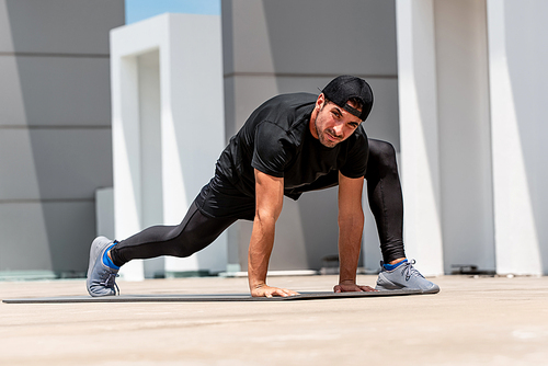 Fit handsome sports man warming up with spider lunge exercise outdoors on building rooftop floor