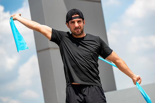 Handsome athletic man stretching with resistance band outdoors on building rooftop, home exercise concept
