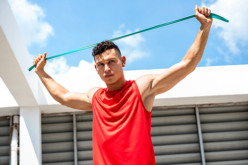 Handsome athletic man stretching with resistance band outdoors on building rooftop, home exercise concept