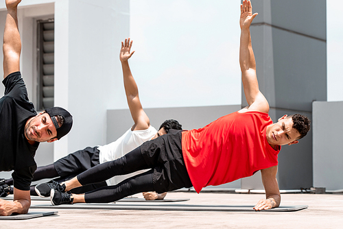 Handsome athletic men doing side plank bodyweight workout training outdoors on building rooftop in sunlight