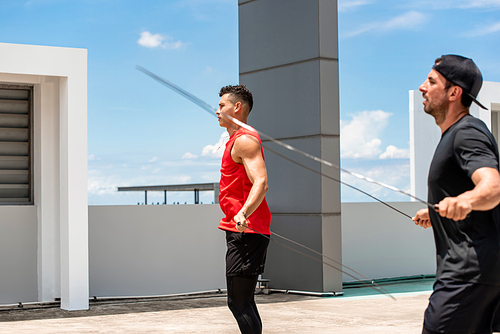 Two handsome Caucasian sportsmen doing morning outdoor exercise jump rope on building rooftop