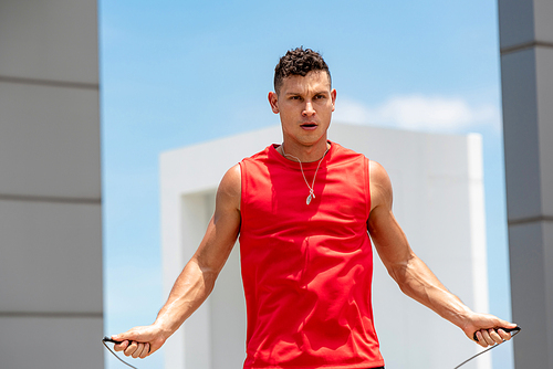 Handsome Caucasian athlete doing morning outdoor exercise jump rope on building rooftop