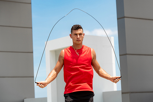 Handsome Caucasian athlete doing morning outdoor exercise jump rope on building rooftop