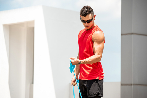 Handsome healthy fit sport man doing bicep curl exercise with elastic resistance band outdoors - home open air workout concept