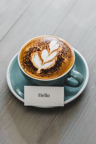 Cup of coffee with latte art and Hello greeting text on vintage wood table in cafe