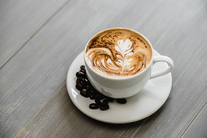 Fresh brewed coffee with fern pattern latte art in white cup on wood tabble