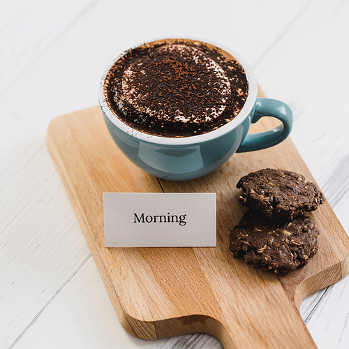 Cup of coffee with dark chocolate cookies and greeting message on wood platter in cafe