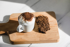 Cup of Babyccino with dark chocolate cookies served on wood platter in cafe