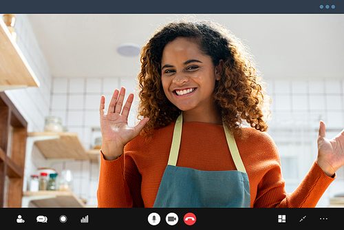 Pretty African American woman smiling and waving hands to the camera while making video call in kitchen at home