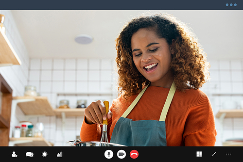 Happy smiling young African American woman making video call while cooking in kitchen at home