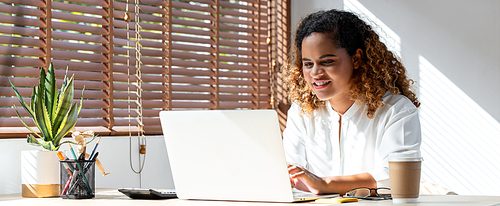 Banner shot of happy young African American business woman working from home on laptop computer in living room