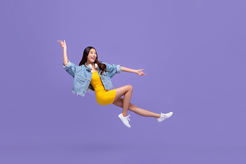 Young beautiful smiling Asian girl floating in mid-air with hand pointing up and down isolated on purple background