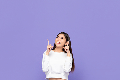Portait of cute smiling young Asian woman pointing hands up and looking at blank space above in purple isolated studio background