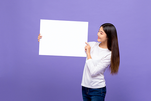 Smiling cheerful Asian woman looking to blank paper isolated on colorful purple background