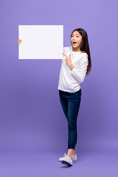 Smiling cheerful Asian woman pointing hand to blank paper board isolated on purple background