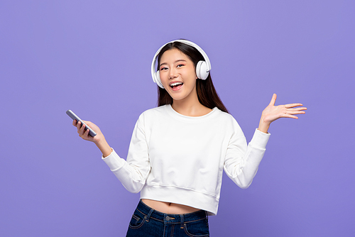 Young pretty Asian woman wearing headphones listening to music from smartphone and opening hand isolated on light purple background