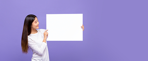 Smiling cheerful Asian woman looking to blank paper board isolated on colorful purple banner background