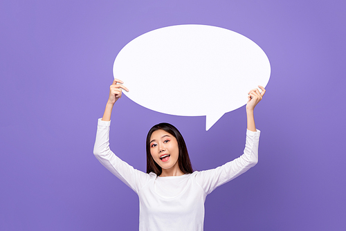 Beautiful Asian woman smiling and holding empty speech bubble isolated on purple background