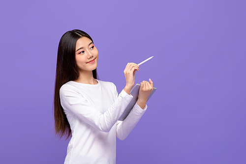 Smart beautiful Asian woman writing on empty space with stylus pen and holding digital tablet isolated on purple background
