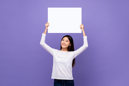 Smiling cute Young Asian woman holding white paper placard with empty space for text overhead