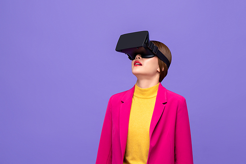 Woman in colorful attire raising head and watching 3D simulation video from virtual reality or VR glasses on purple background